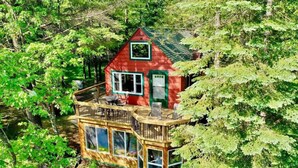 A cabin with a deck, surrounded by trees.