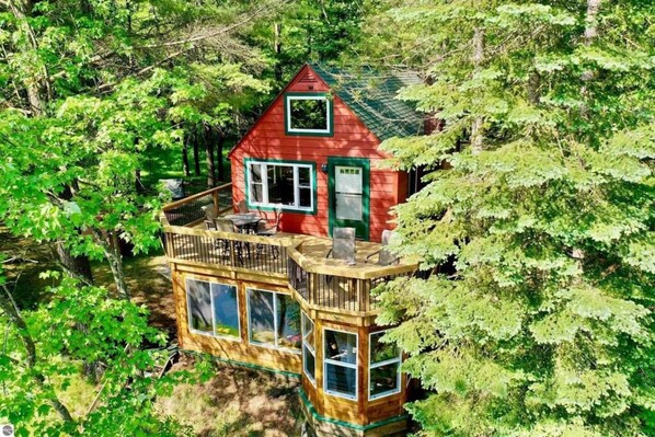A cabin with a deck, surrounded by trees. - Secluded Riverfront Cottage | Sauna, Fire & Kayaks (Evart)