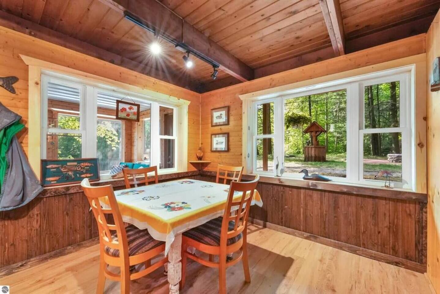 Een houten hut met een eethoek, inclusief een tafel en stoelen, grote ramen en uitzicht op het omliggende bos.