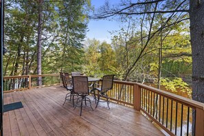 A wooden deck with a table and chairs overlooking a forested area. - Secluded Riverfront Cottage | Sauna, Fire & Kayaks (Evart)