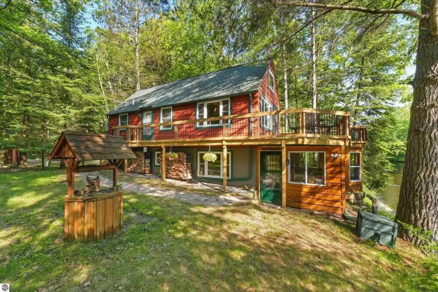 A two-story log cabin with a balcony, surrounded by a forested area.