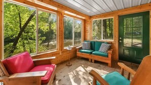 A cozy cabin interior with large windows, a wooden ceiling, and a green door.