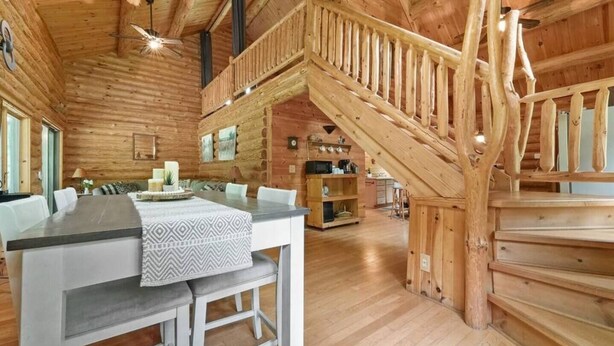 A wooden cabin interior with a dining area, kitchen, and a staircase leading to an upper level. - Secluded | Sauna, Fire Pit & 20 Acres of Trails (Evart)