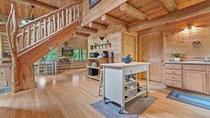 A wooden cabin interior with a wooden staircase, a kitchen area with cabinets and a sink, and a dining area with a table and chairs. - Secluded | Sauna, Fire Pit & 20 Acres of Trails (Evart)