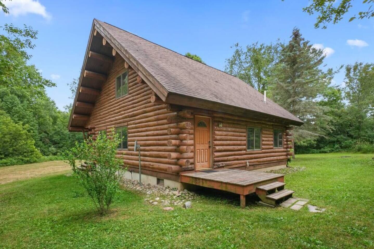En timmerstuga med ett brant tak, en veranda och en liten trädgård framför huset.