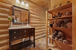 Ein Badezimmer einer Holzhütte mit Waschbecken, Spiegel und Regalen mit aufgerollten Handtüchern.