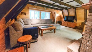 A cozy loft-style living room with a sofa, a coffee table, and a television. - A-Frame | Hot Tub, Fireplace, River, Kayaks &Tubes (Sears)