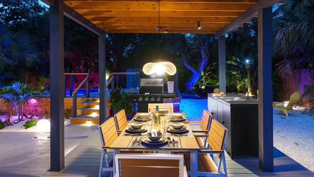 Ein Essbereich im Freien mit einer Holz-Pergola, einem Grill und einem Pool.
