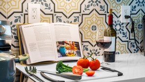 Eine Küchenarbeitsplatte mit Kochbuch, einer Weinflasche und frischen Tomaten und Brokkoli.