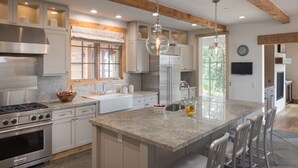 A modern kitchen with granite countertops, stainless steel appliances, and a large island with bar stools. - Outpost: Granite Ridge Chateau (Teton Village)