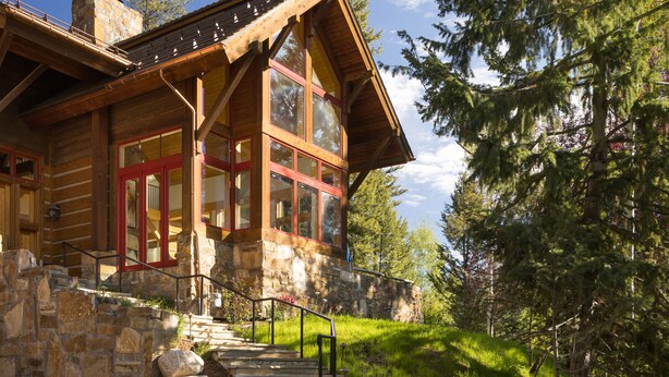 A log cabin with a stone foundation, large windows, and a red door. - Outpost: Granite Ridge Chateau (Teton Village)
