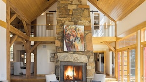 A spacious living room with a stone fireplace, wooden beams, and a high ceiling. - Outpost: Granite Ridge Chateau (Teton Village)
