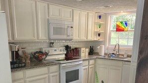 A kitchen with white cabinets, a microwave, a stove, and a sink. There is a cactus plant in the corner. - Lakefront cottage on rustic setting in cove (Buckhead)