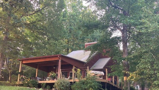 A rustic cabin with a wooden deck and a metal roof, surrounded by trees and a grassy area. - Lakefront cottage on rustic setting in cove (Buckhead)
