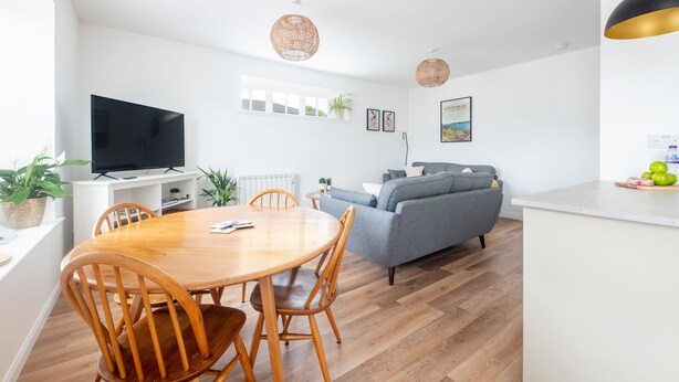 Ein modernes Wohnzimmer mit einem grauen Sofa, einem Holzesstisch und einem Flachbildfernseher.