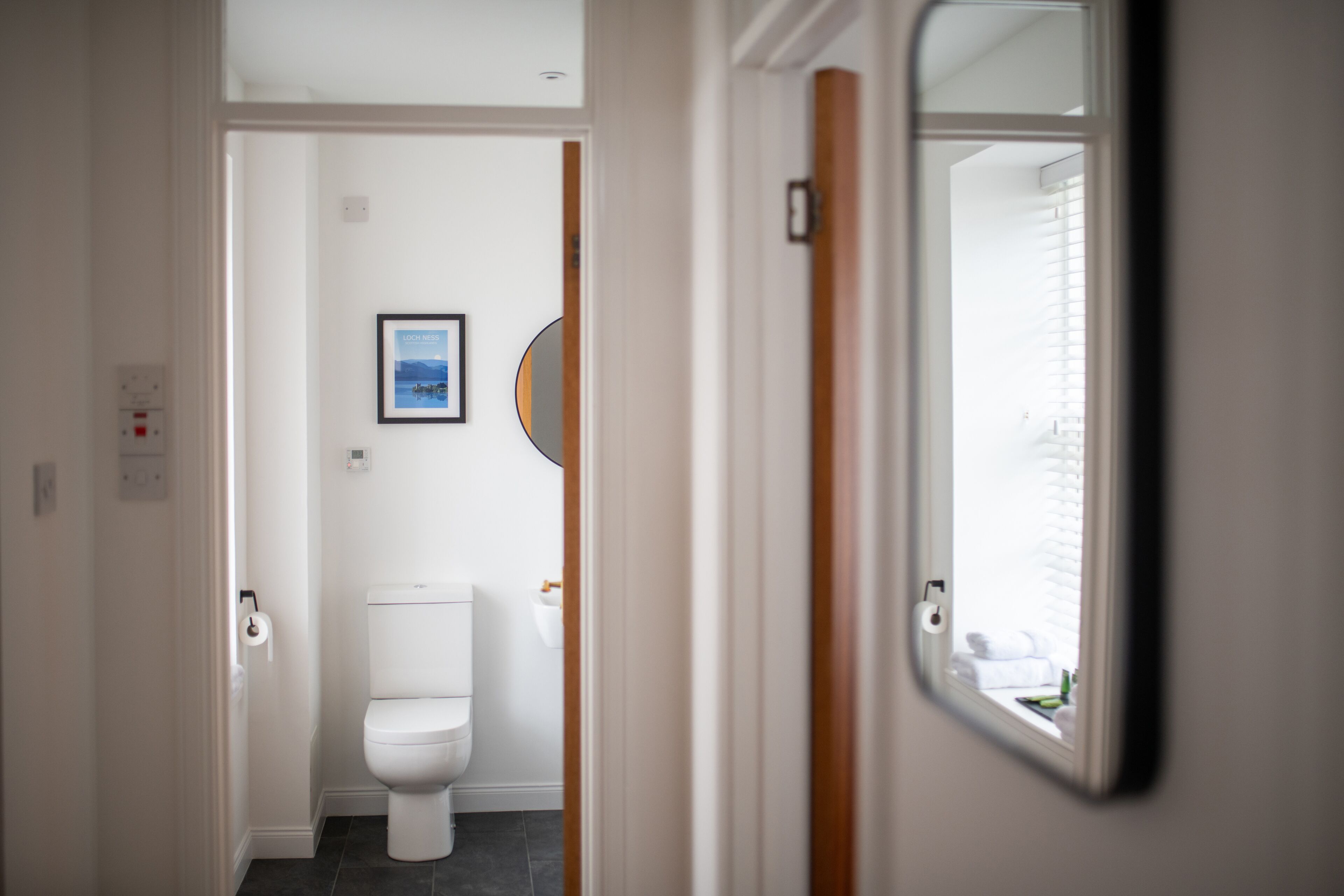 Un pasillo estrecho que conduce a un baño con inodoro, un cuadro en la pared y un espejo en la puerta.