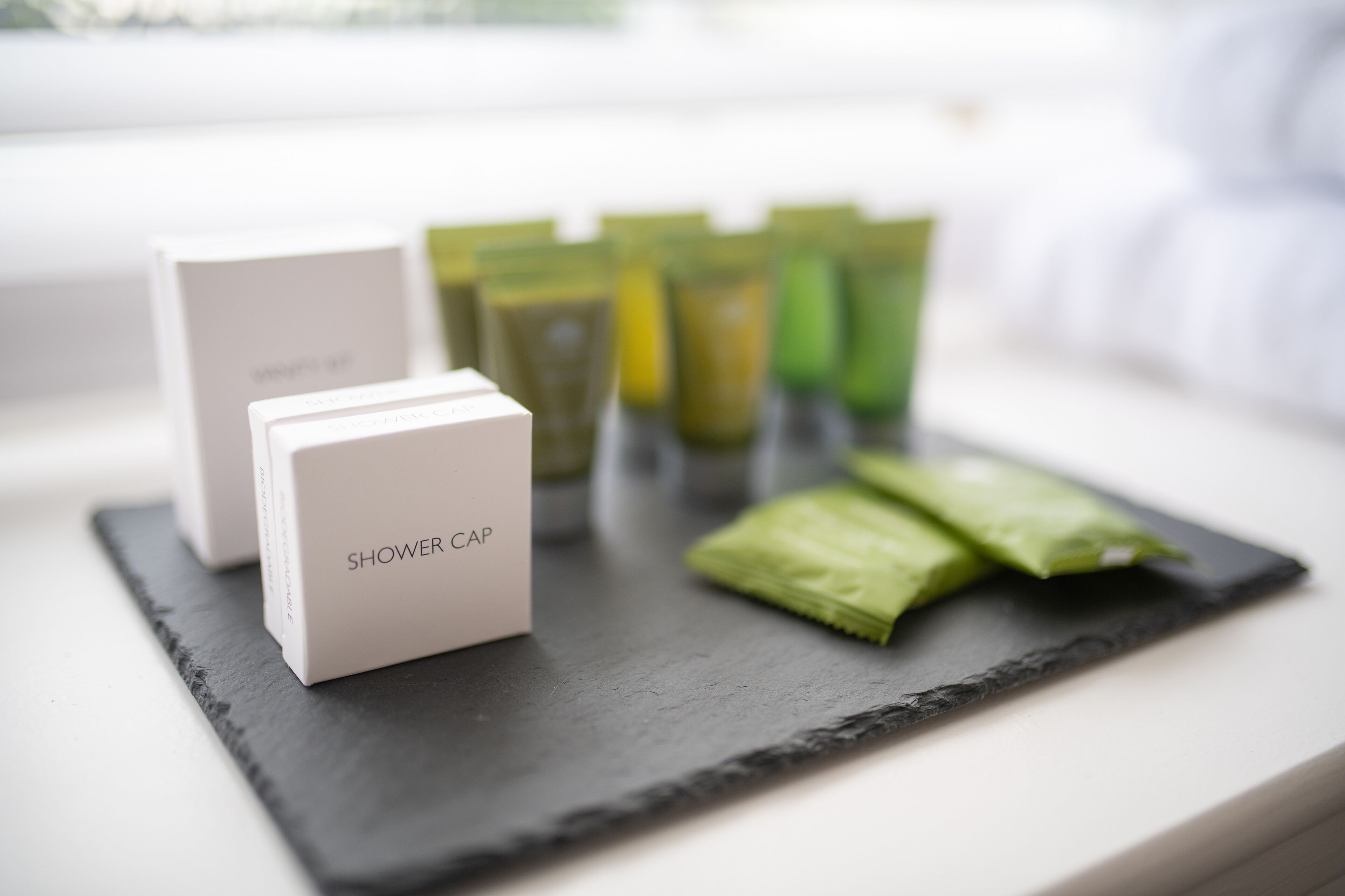 A set of shower caps and green tea packets on a black slate surface.