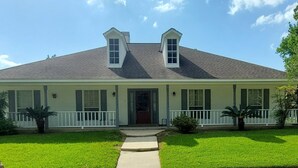 Uma casa de dois andares com varanda da frente, porta central e pequeno jardim frontal.