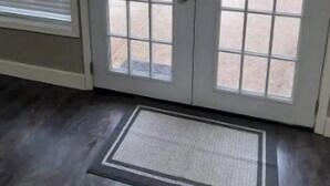 Um quarto com piso de madeira escura, porta branca com painéis de vidro e vista para um gramado verde e um edifício ao fundo.