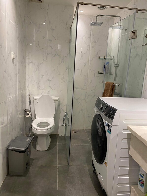 A modern bathroom with a glass-enclosed shower, a toilet, and a front-loading washing machine.