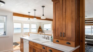 A kitchen with wooden cabinets, a white countertop, and pendant lights. - Right on the Lake Michigan - walk to town and across from TART trail (Suttons Bay)