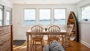 A dining area with a table and chairs, large windows with a view of the sea, and a wooden shelf with books and a toy. - Right on the Lake Michigan - walk to town and across from TART trail (Suttons Bay)