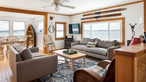 A cozy living room with a sofa, chairs, a coffee table, and a fireplace. Large windows offer a view of the outdoors. - Right on the Lake Michigan - walk to town and across from TART trail (Suttons Bay)