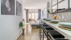 Een moderne eethoek met een lange tafel voor zes personen, een keuken op de achtergrond en uitzicht op de stad door grote ramen.