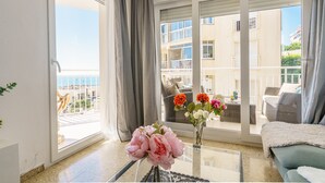 Een balkon met uitzicht op een gebouw en de zee. Er staan twee vazen met bloemen op het balkon.