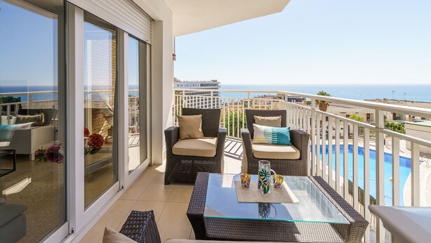 Een balkon met rieten meubels, een glazen tafel en uitzicht op zee.