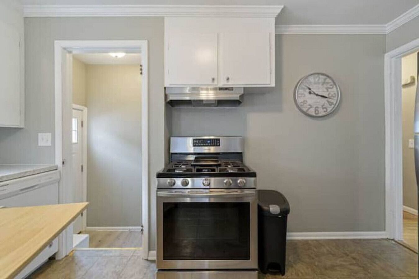 A kitchen with a stainless steel stove, oven, and white cabinets. A clock is on the wall.