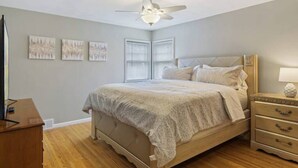 Ein Schlafzimmer mit einem Bett, einem Nachttisch, einem Deckenventilator und Kunstwerken an der Wand.