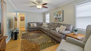 Ein Wohnzimmer mit einem Ecksofa, einem Couchtisch, einem Teppich, einem Deckenventilator und einem Gemälde an der Wand.
