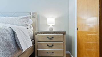 Quarto com cama, mesa de cabeceira e abajur, e porta de madeira.