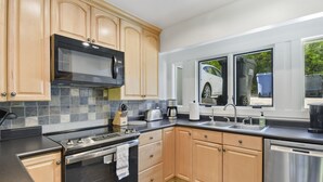 A modern kitchen with wooden cabinets, a stainless steel microwave, a Bosch dishwasher, and a window with a view of a car and trees.