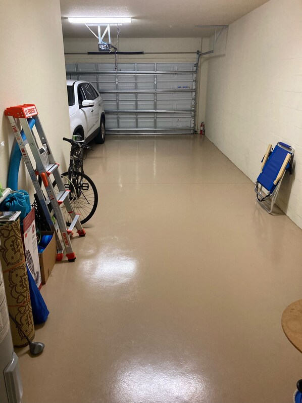 Garagem com um carro branco estacionado, uma bicicleta e uma cadeira dobrável azul.