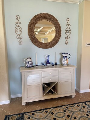 A white cabinet with a mirror above it, flanked by decorative wall sconces, and a patterned rug on the floor.