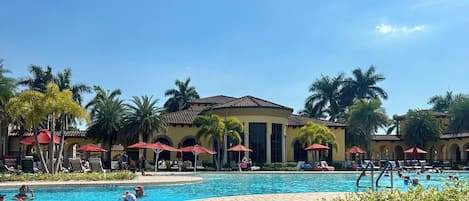 A pool area with lounge chairs and umbrellas, surrounded by palm trees and a building with arches.