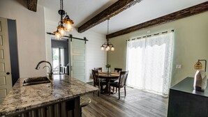 A kitchen with a granite countertop, wooden dining table, and chairs. There is a hanging light fixture above the counter. - Modern Holistic Home - Near the Village & Shopping!  (Meridian)