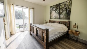 A bedroom with a wooden bed, a ceiling fan, a nightstand with a lamp, and a sliding glass door leading to an outdoor area. - Modern Holistic Home - Near the Village & Shopping!  (Meridian)
