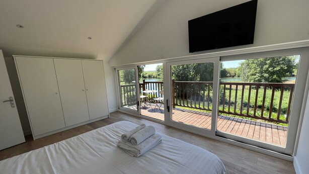 A bedroom with a large bed, a wardrobe, a TV, and a sliding glass door leading to a deck with a view of greenery. - Casa Belavista, seine view and jacuzzi (Connelles)