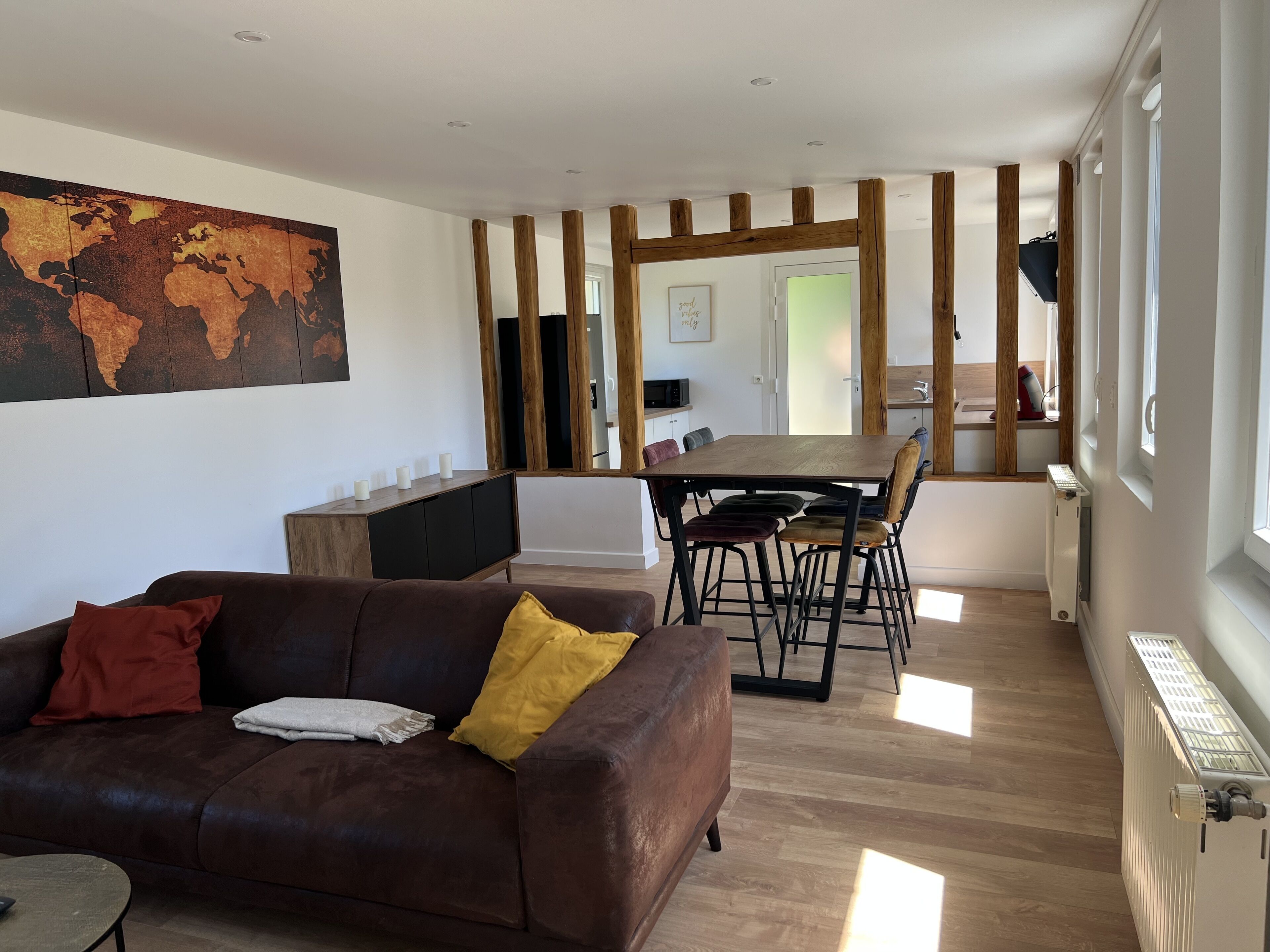 Un salon moderne avec un canapé en cuir marron, une table à manger en bois et une grande carte du monde accrochée au mur.
