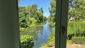 A view through a window of a river with surrounding greenery and a hedge. - Casa Belavista, seine view and jacuzzi (Connelles)