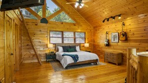 A wooden cabin bedroom with a bed, nightstands, a dresser, a guitar, and a ceiling fan. - Modern Cabin w/ Hot Tub - 17 min to Dollywood (Sevierville)