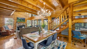 A wooden interior with a dining table set for four, a staircase, and a living area with a sofa and a television. - Modern Cabin w/ Hot Tub - 17 min to Dollywood (Sevierville)