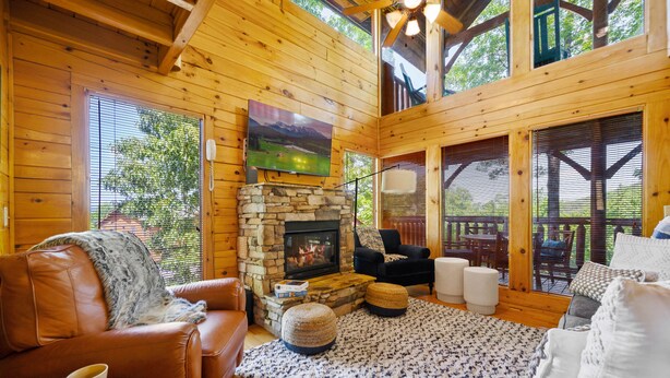 A cozy cabin interior with a stone fireplace, leather sofas, and a large TV mounted above it. - Modern Cabin w/ Hot Tub - 17 min to Dollywood (Sevierville)
