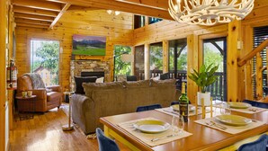 A wooden cabin interior with a dining table set for four, a sofa, and a fireplace. - Modern Cabin w/ Hot Tub - 17 min to Dollywood (Sevierville)