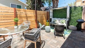 Un patio con mobiliario de mimbre, una mesa de vidrio y una pared verde.