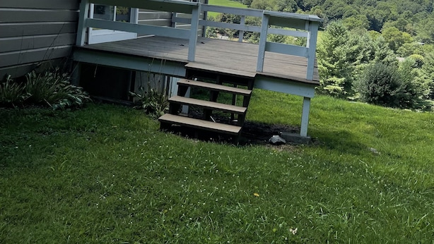 A house with a wooden deck and a white railing, surrounded by lush green grass and trees. - We are located in the beautiful blue ridge mountains (Sparta)