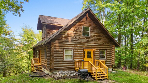 A log cabin with a wooden porch, a grill, and a number '982' on the door.